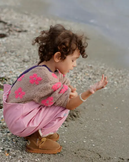 Meisje waterdichte kleren op het strand herfst spelen met zand